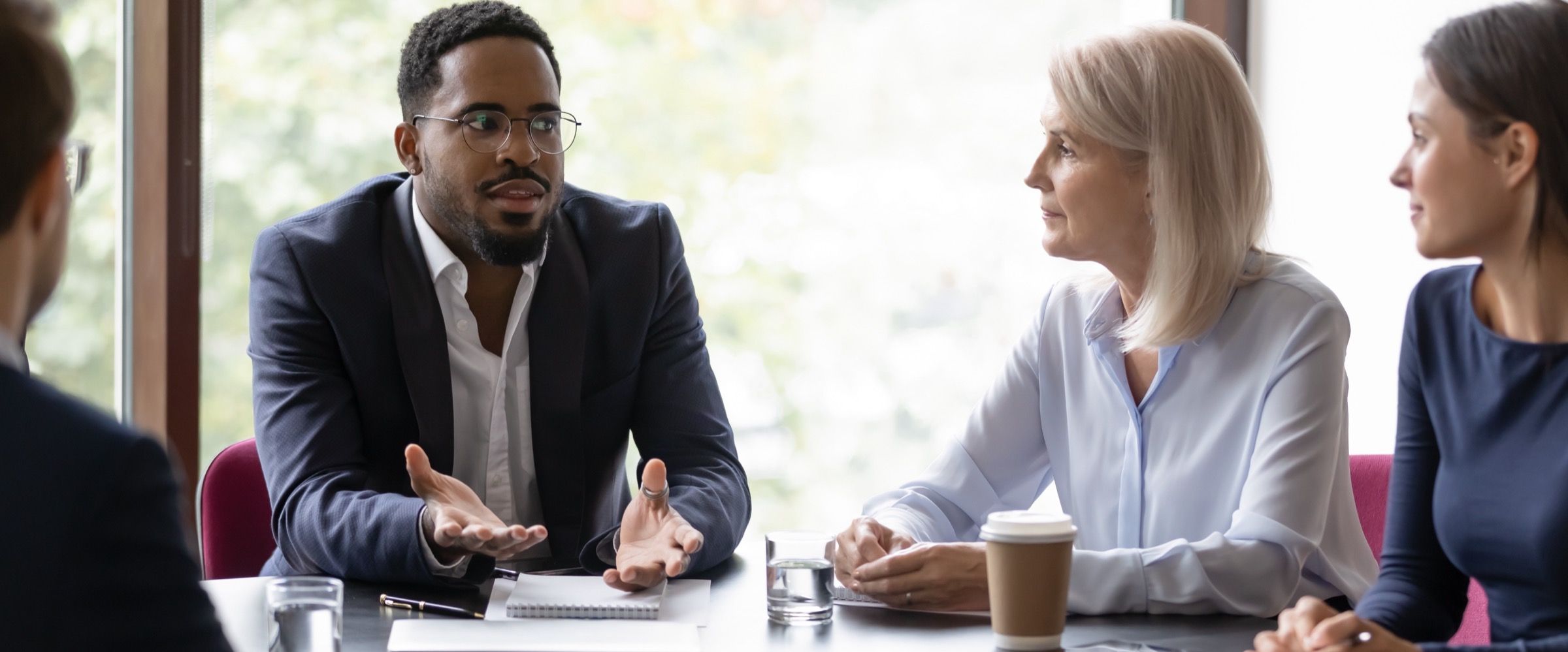 A trainer speaking with a group seated around a meeting table.